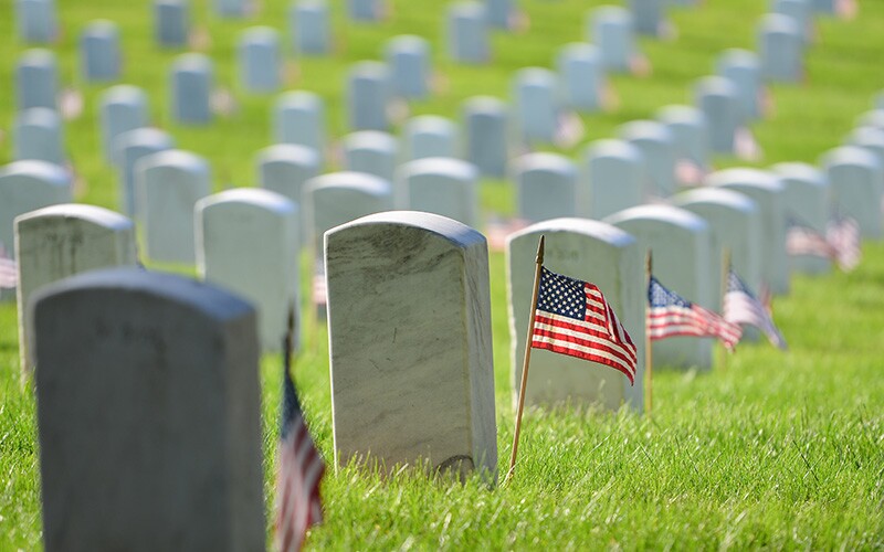 Gravestones at Arlington National Cemetery with military flags by them.