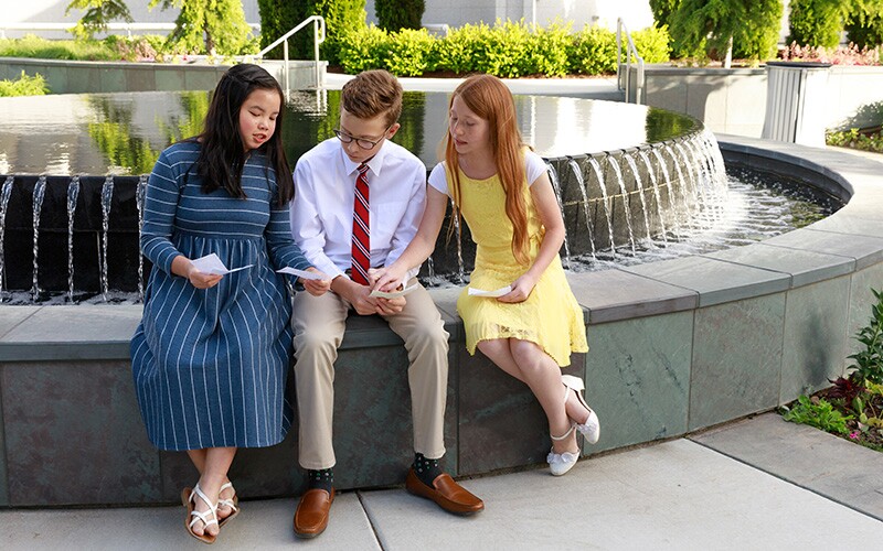 Teenagers sitting on a temple bench looking at temple ordinance cards.