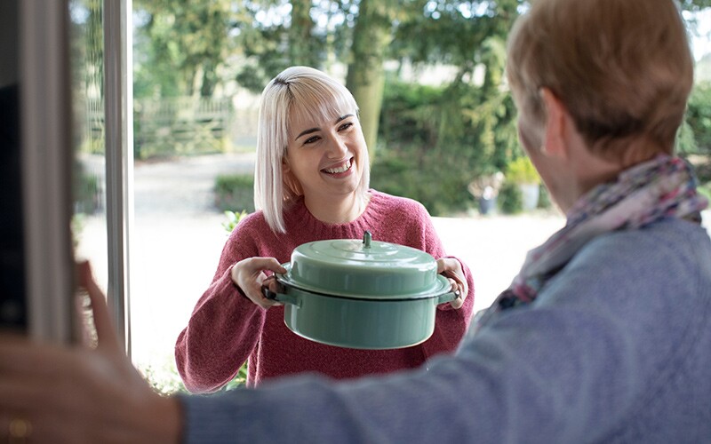 Blonde woman bringing food to an elderly neighbor.