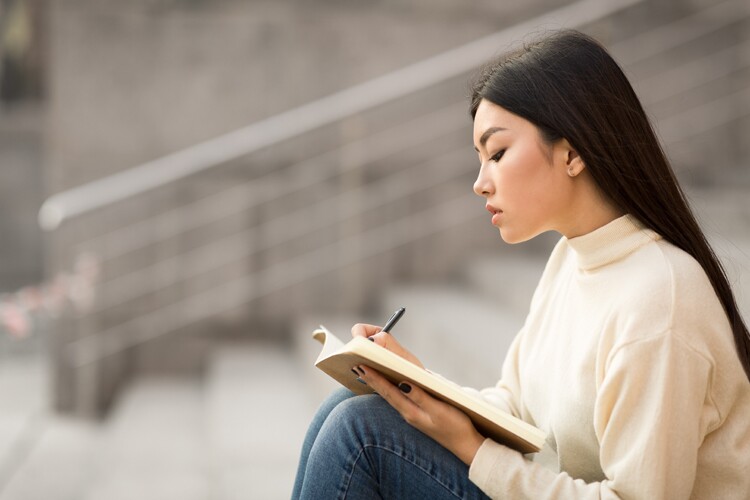 woman writing in her anxiety journal while sitting on outside steps