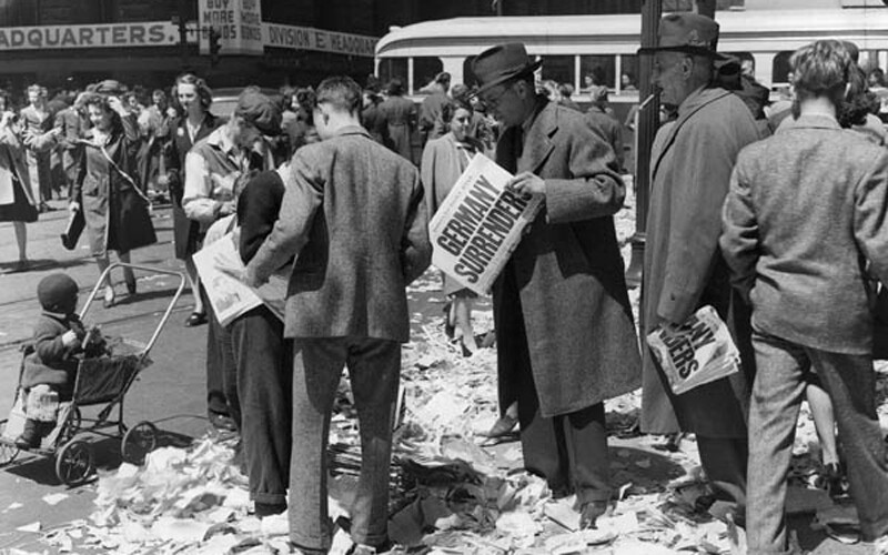 Men hold newspaper reading "Germany Surrenders", signaling a turning point in WW2