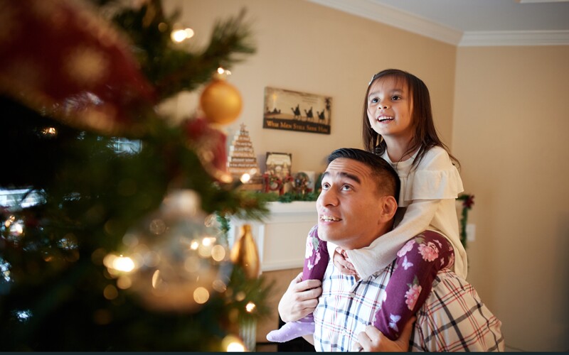 a father and daughter decorate a christmas tree together.