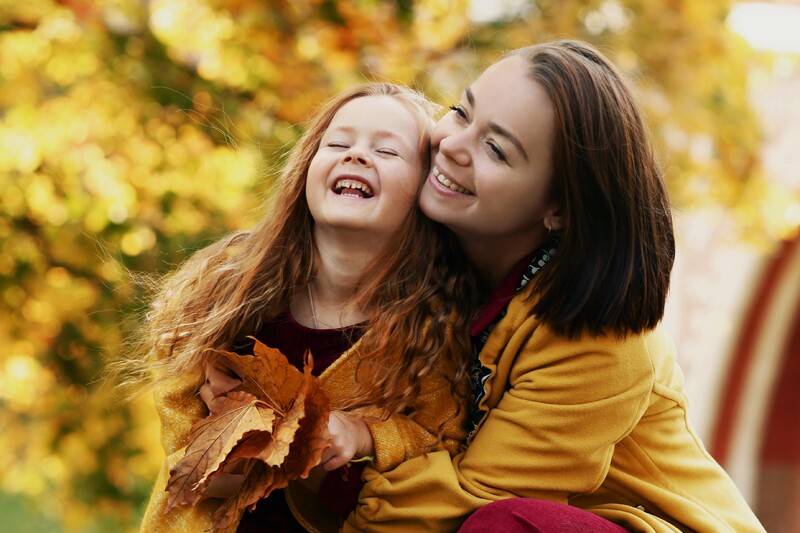 an irish mom and a little girl laugh together in the leaves.
