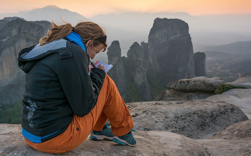 Girl writing in a travel journal on a mountain.