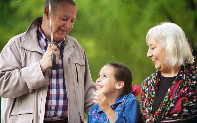 Grandparents holding an umbrella with a little girl.