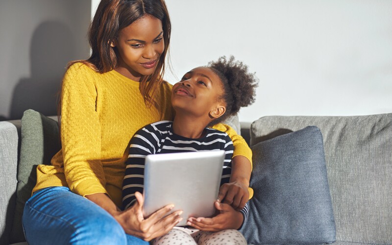 an african american woman and her daughter read on a tablet together