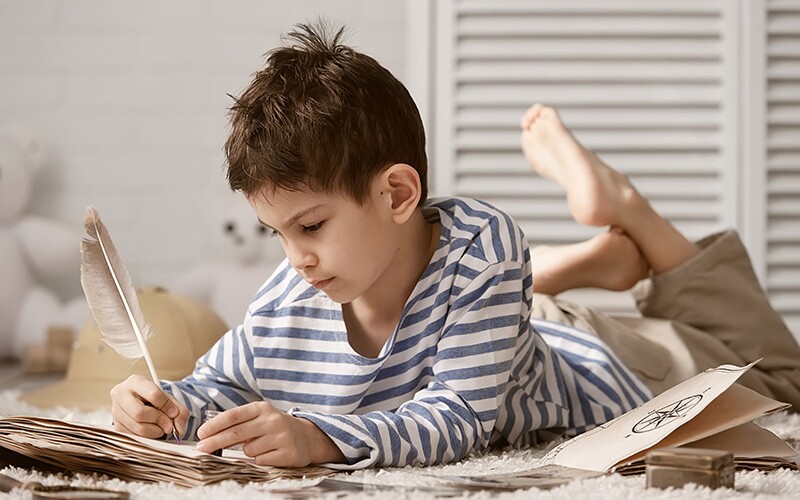 Little boy journaling on the floor with a feather pen.