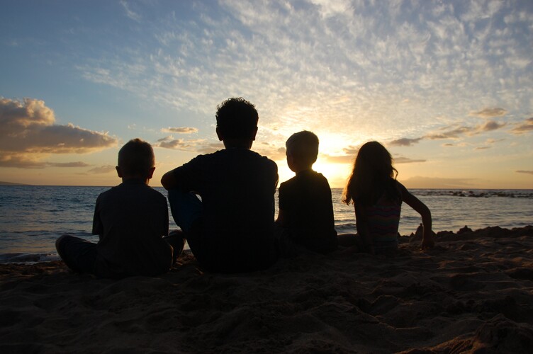 children on a beach look out to the ocean during sunset.