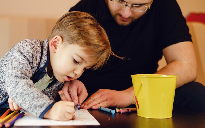 Little boy draws while father helps him