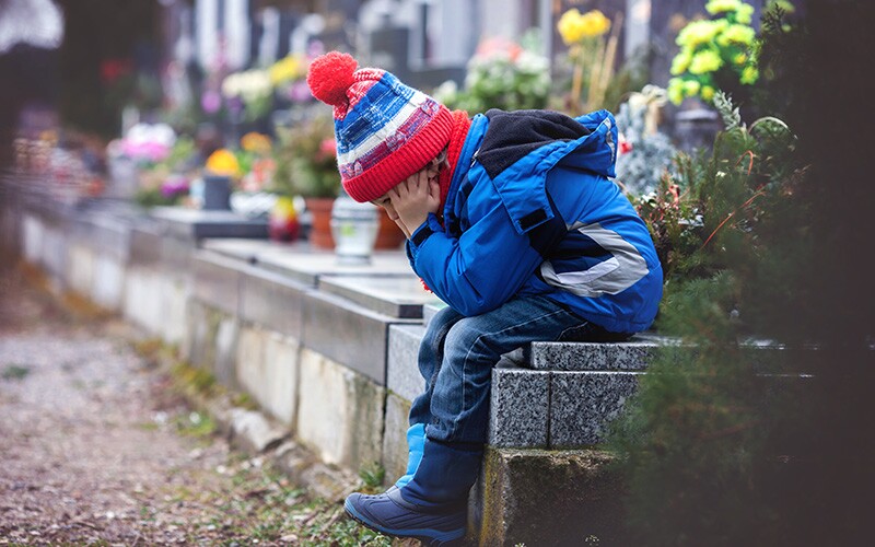 Little boy mourning and sitting on a grave.