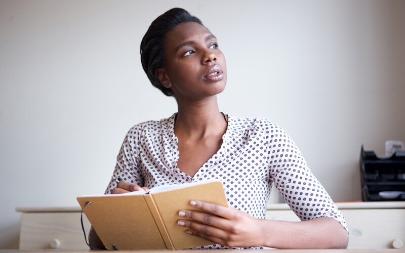 woman holding a journal looking off in the distance