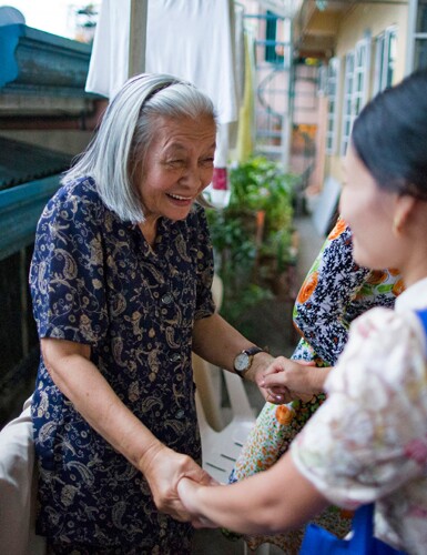 An elderly woman smiles at another woman 