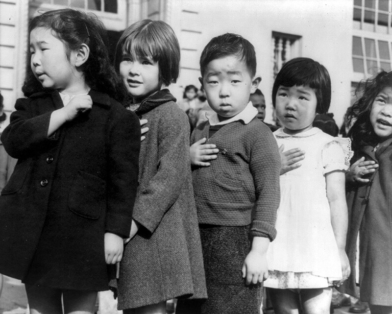 Japanese children hold their hands over their hearts and pledge allegiance to the united states during ww2.