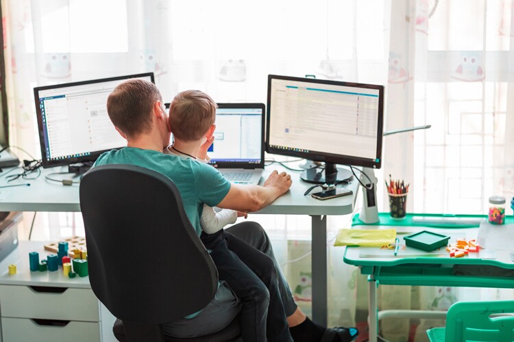 father works from home on computer and has son in his lap