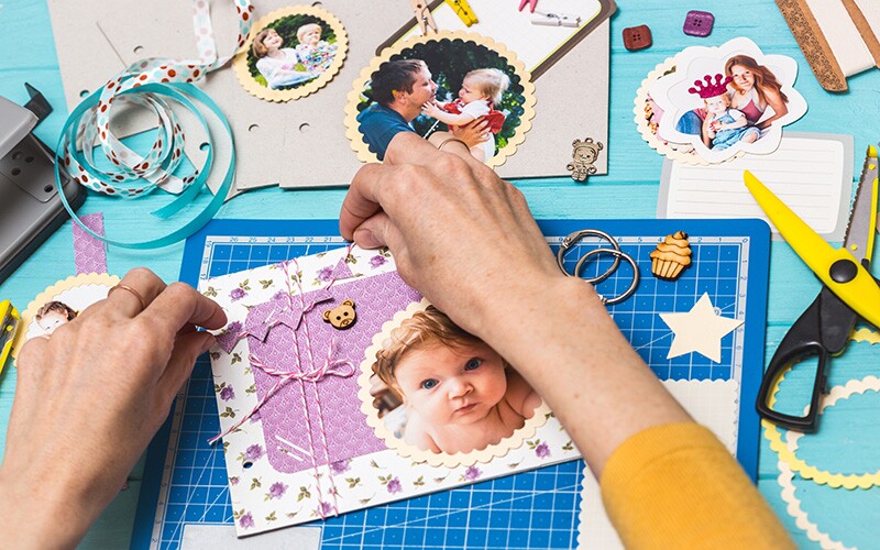 Creating a baby scrapbook with cut out pictures, stickers, and ribbons.