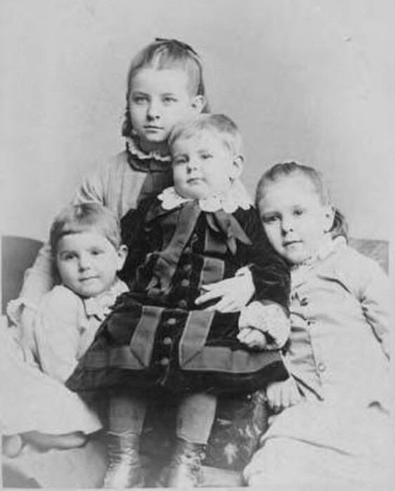 Four children wearing 1870s children's clothing.