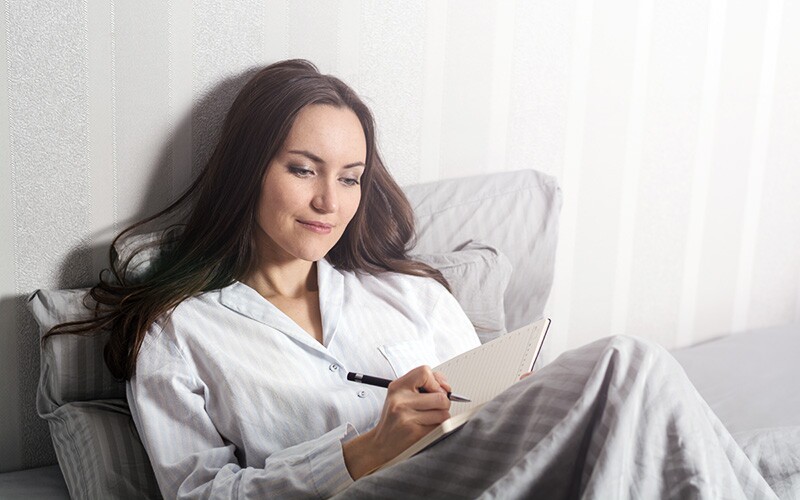 Girl in bed writing her dreams in a dream journal.