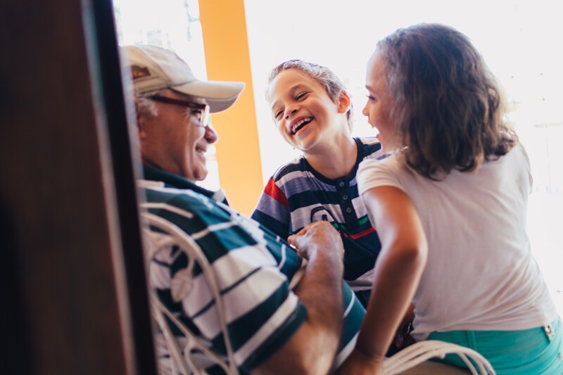 Un niño y una niña riendo con su abuelo. Descubre cómo llamar a los abuelos